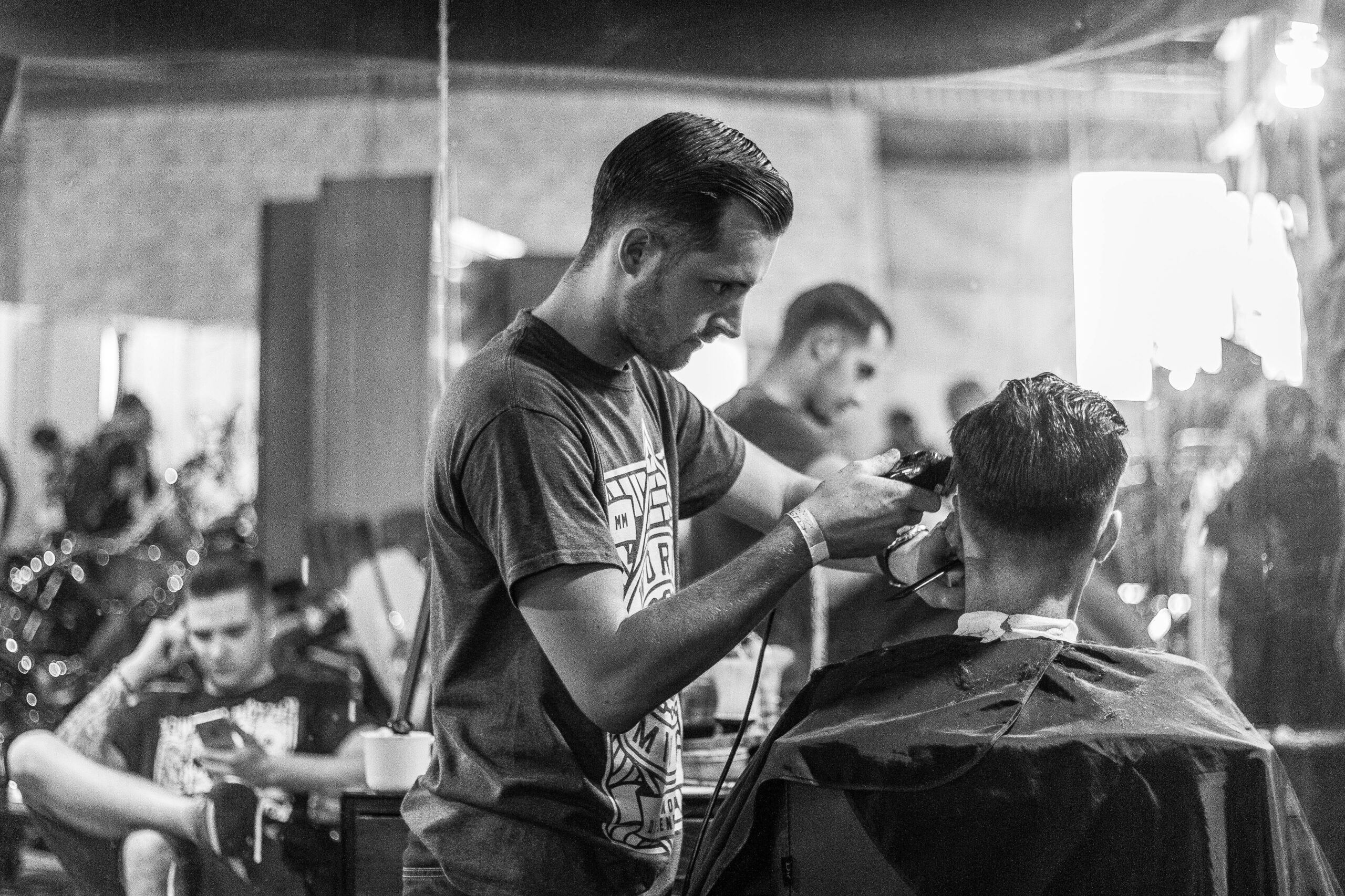 A barber skillfully gives a haircut in a stylish Wrocław barbershop, captured in moody monochrome.